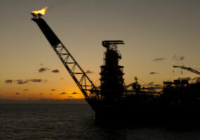 Silhouette of an FPSO oil rig bow at sunset/sunrise time, with flare burning gas.